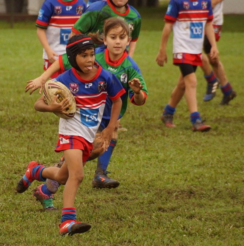 Ivanhoes junior player makes a run with the ball during a muddy game of footy. 